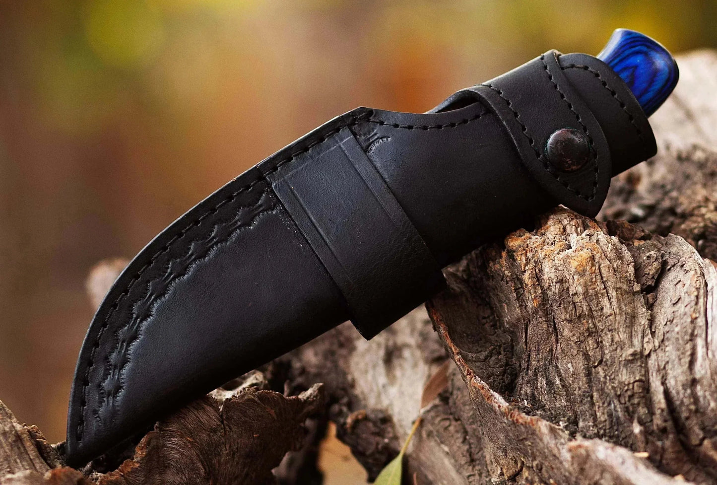 Damascus Steel Hunting Knife with leather sheath on wood background.
