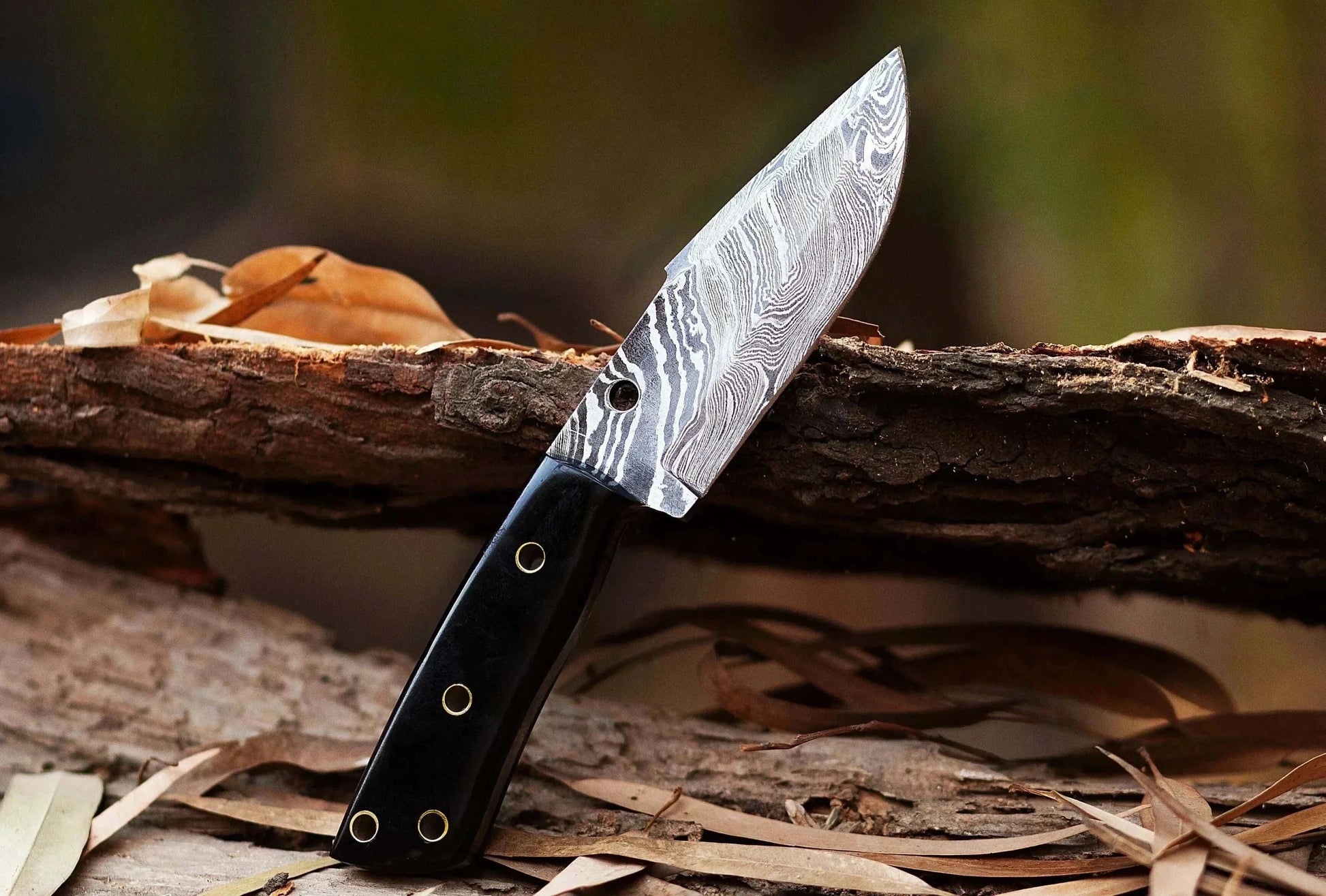 Damascus Steel Hunting Knife with patterned blade and bull horn handle on a wooden surface.