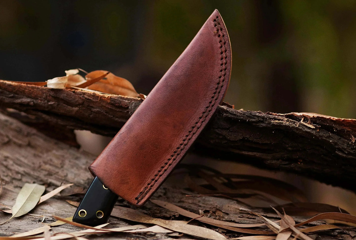 Damascus Steel Hunting Knife with leather sheath on a log.
