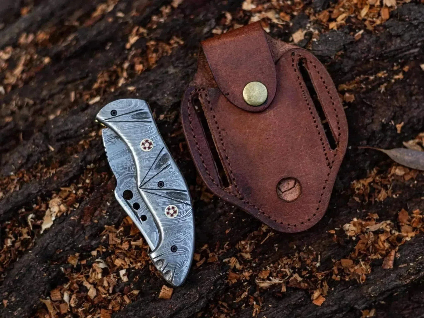Damascus Steel Folding Knife with leather sheath on wooden surface.