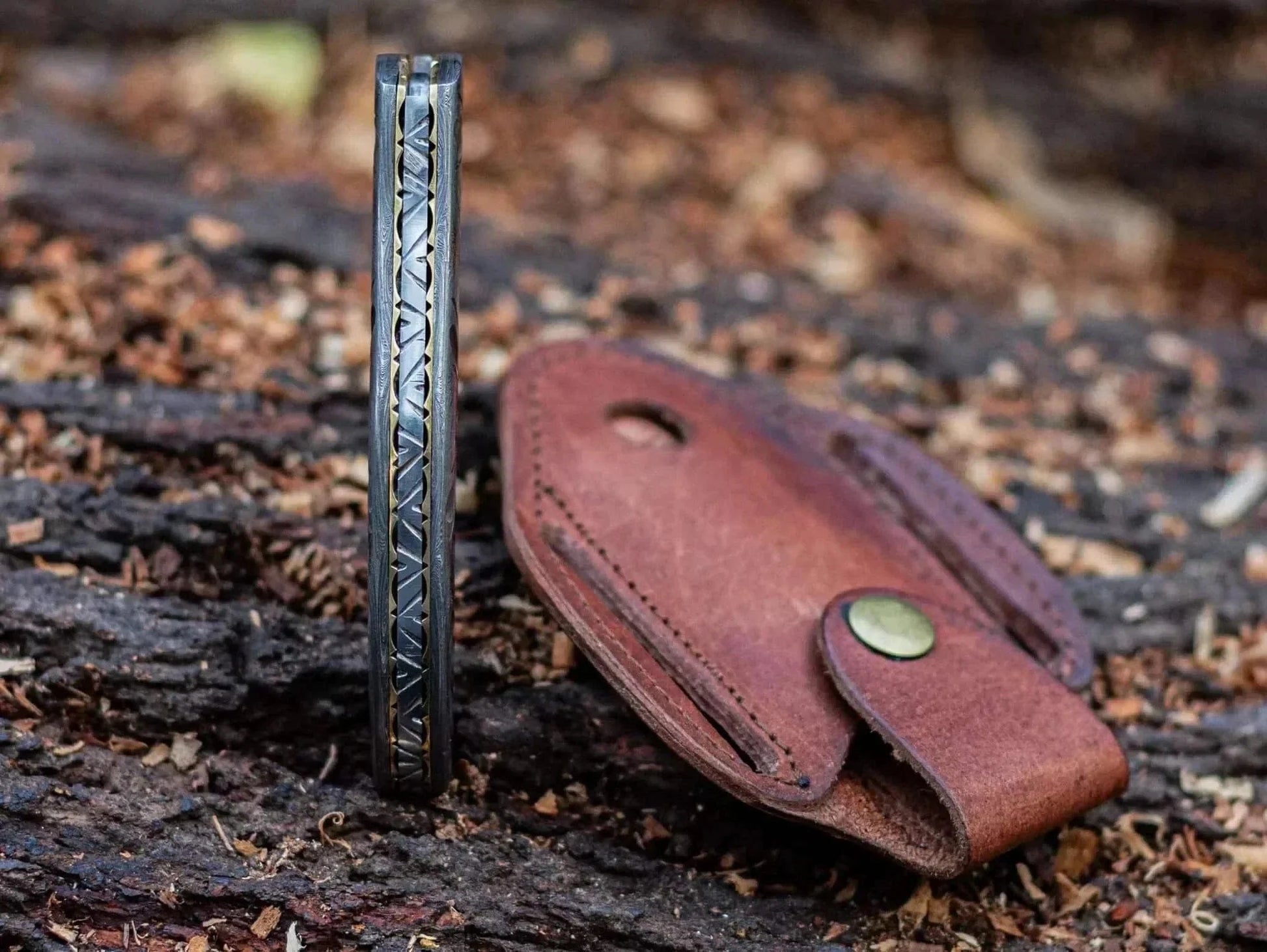 Damascus Steel Folding Knife with leather sheath on a wood background.