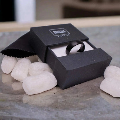 Matte black tungsten ring in elegant black box with cleaning cloth and packaging peanuts.