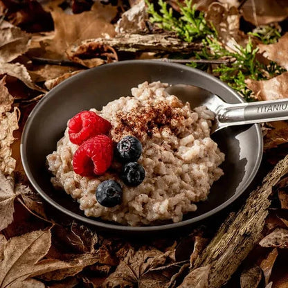 Coconut rice pudding with berries on a black plate, set on outdoor leaves.