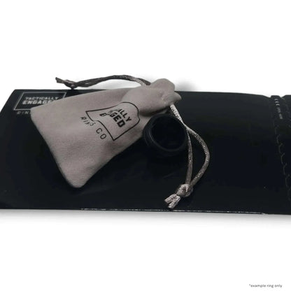 Black silicone ring with a unique centered trench and beveled edges, placed beside a branded pouch on a dark surface.