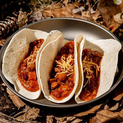 Spicy Mexican Beans in flour tortillas with shredded cheese on a black plate, surrounded by outdoor foliage.