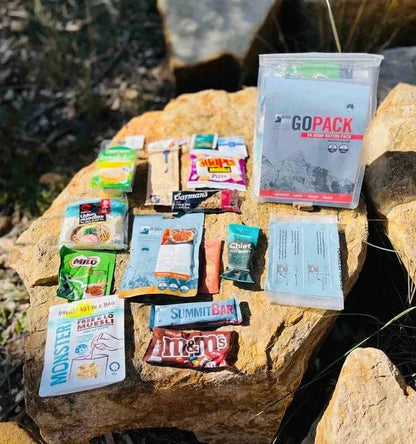 GoPack 24-hour food ration pack with meals, snacks, and drinks on rocks outdoors. Ideal for camping and hiking adventures.