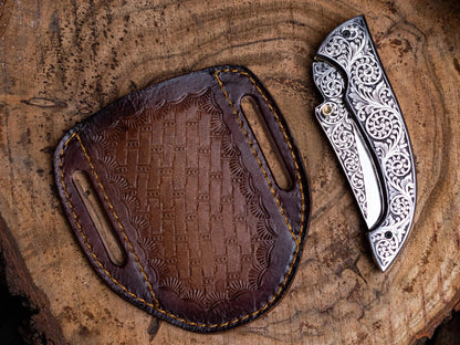Premium lockback utility knife with engraved stainless steel handle and leather sheath on wood surface.