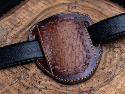 Stainless steel folding knife with engraved design and leather sheath on wooden surface.