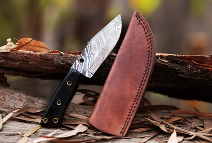 Damascus Steel Hunting Knife with leather sheath on a wooden surface.