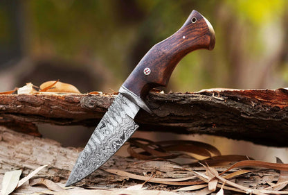 Damascus Steel Hunting Knife with rose wood handle on tree trunk, showcasing patterned blade.