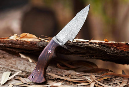 Damascus Steel Hunting Knife with rosewood handle and patterned blade on a log.