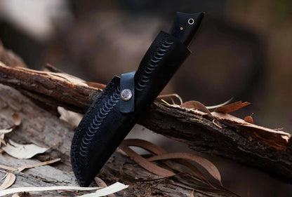 High carbon steel hunting knife with leather sheath on wood.