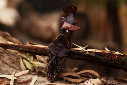 Damascus Steel Hunting Knife with leather sheath, rosewood handle, and forged blade displayed on wood.