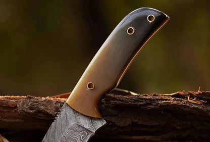Damascus Steel Hunting Knife with bull white horn handle, featuring a pattern welded blade on wooden surface.