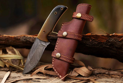 Damascus Steel Hunting Knife with bull horn handle and leather sheath on rustic background