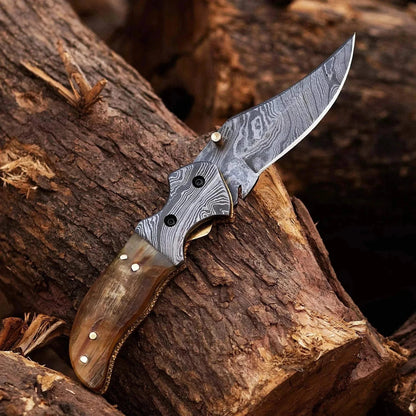 Damascus Steel Folding Knife with Ram White Horn handle on wooden surface.
