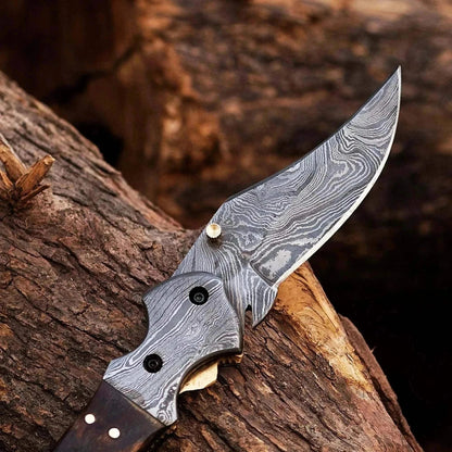 Damascus Steel Folding Knife with distinctive patterned blade and ram black horn handle on wooden surface.