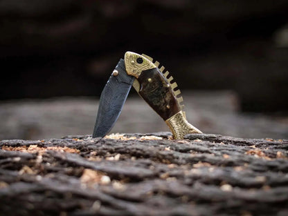 Fish Style Damascus steel folding knife with bone and brass handle on textured surface.