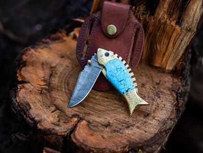 Fish Style Damascus Steel Folding Knife with Leather Sheath on Wooden Surface.