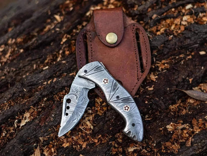 Damascus Steel Folding Knife with leather sheath on wood background, showcasing intricate blade patterns.