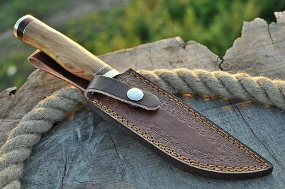 Damascus Steel Hunting Knife with leather sheath on rustic surface.