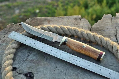 Damascus Steel Hunting Knife with wooden handle, next to a ruler on a wooden surface.